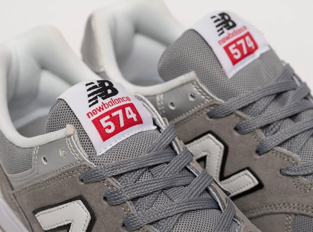 Cette chaussure est la New Balance Numeric 574 Vulc (référence couleur Grey/White), modèle classique iconique de la marque américaine New Balance