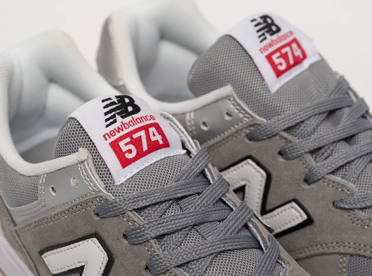 Cette chaussure est la New Balance Numeric 574 Vulc (référence couleur Grey/White), modèle classique iconique de la marque américaine New Balance