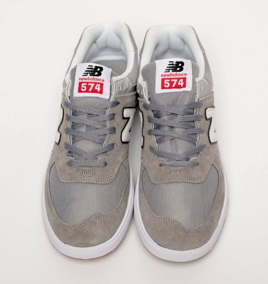 Cette chaussure est la New Balance Numeric 574 Vulc (référence couleur Grey/White), modèle classique iconique de la marque américaine New Balance