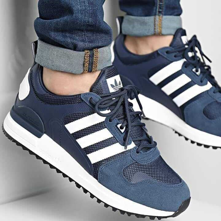 Le modèle présenté dans l'image est la adidas ZX 700 HD dans son coloris bleu marine classique avec les trois bandes blanches caractéristiques de la marque adidas.