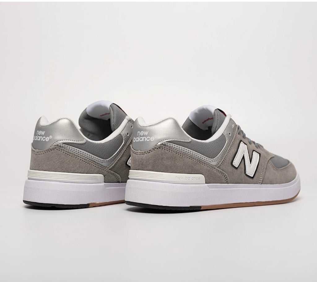 Cette chaussure est la New Balance Numeric 574 Vulc (référence couleur Grey/White), modèle classique iconique de la marque américaine New Balance