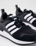 Le modèle présenté dans l'image est la adidas ZX 700 HD dans son coloris bleu marine classique avec les trois bandes blanches caractéristiques de la marque adidas.