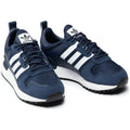 Le modèle présenté dans l'image est la adidas ZX 700 HD dans son coloris bleu marine classique avec les trois bandes blanches caractéristiques de la marque adidas.
